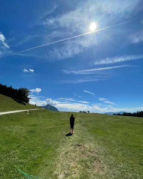 Wanderin mit Stöcken auf einer weiten Almwiese unter blauem Himmel