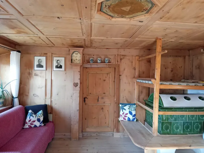 Die Bauernstube mit grünem Kachelofen, getäfelter Decke und rotem Sofa